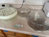 All four items grouped on countertop: metal/plastic cake taker with glass plate on top, salad bowl, Rubbermaid container