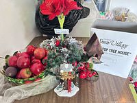 Lot overview showing basket of plastic apples, faux floral centerpiece, Snow Village treehouse and box, partial birdhouse