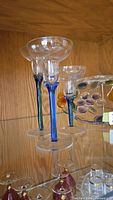 front view of three tall candle glasses with coloured stems and glass tray behind