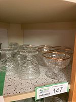 Group of twelve glass cups on shelf, showing two distinct sets