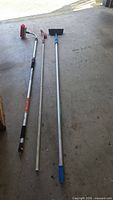Three long handled hose brushes laid side by side showing full length, pole materials, grips and brush heads