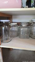 Four pickle jars on shelf, mix of square and round, lids visible