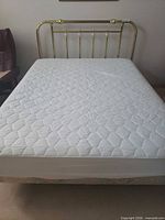 Full view of assembled queen brass bed frame with mattress for scale