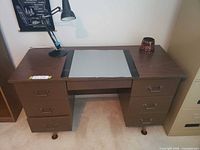 Front view of brown 7-drawer desk with lamp, pencil holder and blotter displayed on top