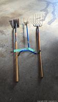 three yard tools laid out: spade, tiller, pitchfork