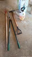 Four garden tools laid out: cultivator rake, hedge shears, edger, sprayer