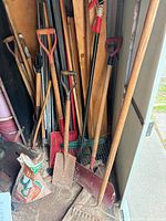 Cluster of shovels, rakes, stakes, scoop shovel and soil bag in shed corner