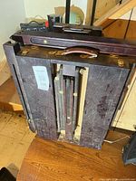 Folded wooden easel showing leather handle and brass hardware