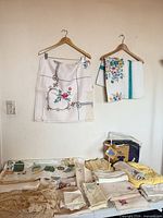 Overview of hanging embroidered tablecloths and stacks of assorted linens on table