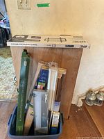 Overview of lot showing TV mount box atop wood panel, gutter guard box, packaged blinds, rods, diffuser, panel and excluded bin