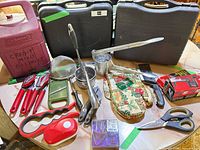 Overview of lot showing stoves in cases, lantern case, and assorted kitchen tools