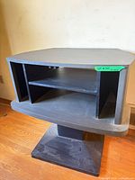 Front view of black corner TV stand showing shelves and pedestal base