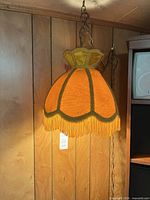 Full view of swag lamp hanging against wood panel, shows shade color, chain, cord
