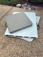 Folded table showing gray hard case stacked on white tabletop with black handles and metal frame visible