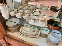 Entire dinnerware set displayed on glass shelf showing cups, coffee pot, sugar, creamer, plates and bowls