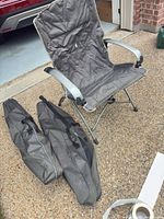 Gray folding camping chair open with two carrying bags on ground
