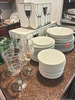 Stacks of white plates and bowls, loose wine glasses in foreground