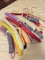 Pile of multicolor satin padded hangers showing variety of colors and metal hooks
