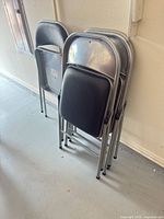 Stack of four folded silver metal chairs with black vinyl seats