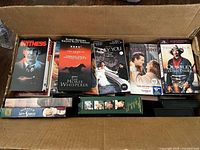 Open carton displaying rows of assorted VHS tapes with visible titles Witness, The Horse Whisperer, Only You, Quigley Down Under, Miracle on 34th Street