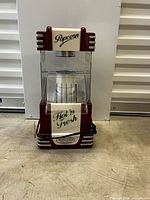 Front view of red Nostalgia Electrics popcorn maker showing housing, kettle, signage and cord