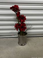 Full view of red artificial amaryllis arrangement in silver pot against backdrop
