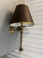 Side view of brass wall lamp mounted showing shade and column stem