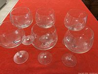 Six clear stemmed wine glasses on red surface