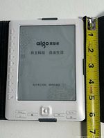 Front of white aigo e-reader in case with ruler showing screen size