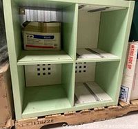 Front view of light green 2x2 Kallax showing four cubbies, hardware, back panels