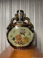 Front view of flattened porcelain moon flask vase displaying peony and butterfly panel, dragon handles, gilt decoration