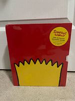Front view of red slipcase with Bart hair graphic and round yellow sticker