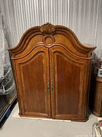 Front view of closed entertainment center showing arched carved top and double doors