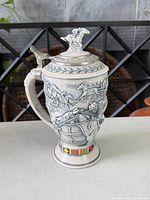 Left profile of stein showing relief scene and pewter lid