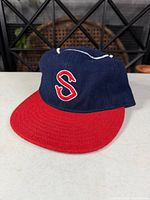 Front view of navy cap showing red bill and embroidered S logo