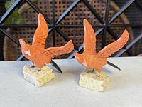 Front view of both orange wood bird figurines on stone bases