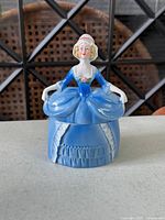 Front view of porcelain powder jar showing figurine lid and blue skirt base