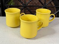 Three yellow ceramic coffee mugs front view