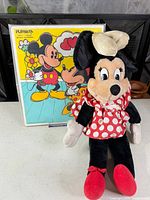 Full view of Minnie Mouse plush standing in front of puzzle box