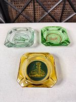 All three ashtrays grouped: clear/light green Fitzgerald's, green Barney's, amber Palace Club