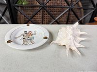 Ashtray and conch shell side by side on tabletop