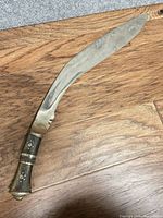 Full view of curved kukri knife on wooden floor showing entire blade and handle