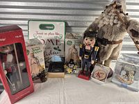Group shot of all holiday décor items including boxed tree topper, boxed nutcracker, loose nutcracker, plush Santa, ornaments, sign and nativity set