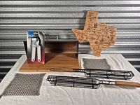 Group shot showing all items: garlic press package, breadbox, Texas board, chainmail scrubbers, two grill baskets