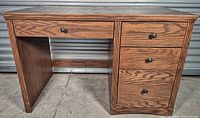 Front view of oak-finish veneer desk showing top drawer, three side drawers, and open knee space