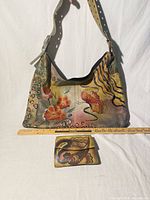 Front view of handbag hanging and wallet placed below with ruler for scale