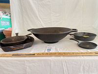 Overall lot showing wok, grill pan and three skillets with ruler for scale