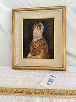 Full view of framed needlepoint portrait with ruler for scale