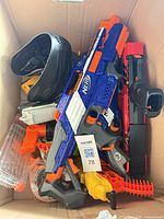 Overview of box contents including blue Elite blaster, black/red blaster, magazines, attachments, and mask