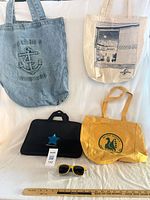 Group shot showing three tote bags, laptop sleeve and sunglasses for scale